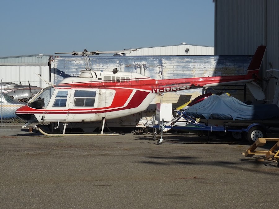 A red and white Bell 206 helicopter parked on the ramp outside the Big Valley Aviation hangar