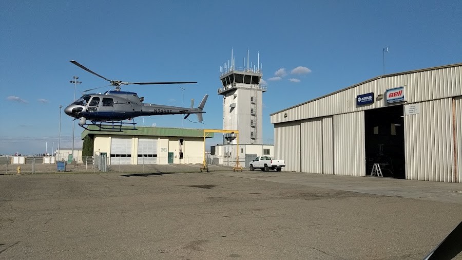 A helicopter lifting off from the ramp beside the Big Valley Aviation hangar and the Stockton airport control tower